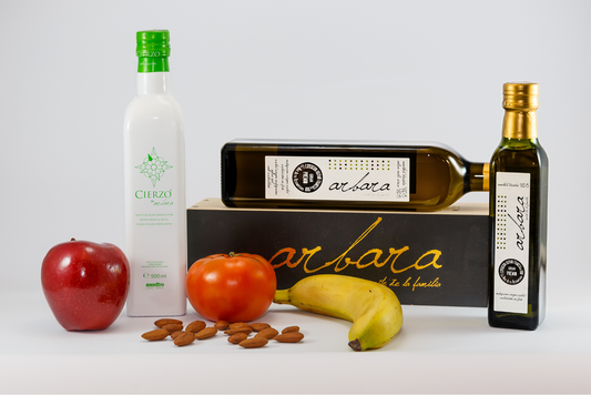 Arbara, botellas de aceite de oliva virgen extra sobre caja de madera con frutas y almendras, fondo blanco.